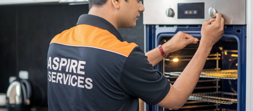 Aspire Services technician in a black uniform repairing the button of a microwave, focused on restoring its functionality with precision.