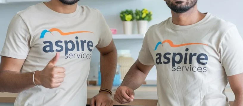 Two Aspire Services technicians wearing cream t-shirts with the Aspire logo stand in front of a washing machine, both giving a thumbs up.